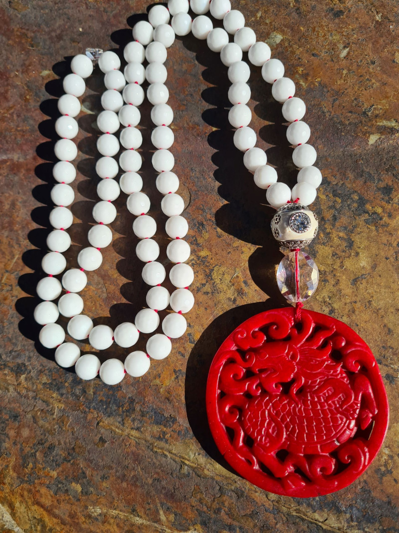 Long necklace of white agates with a red jade medallion and crystal